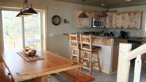 Un tavolo da pranzo in legno con panche, angolo cottura con pensili in legno, un forno a microonde e una sveglia appesa al muro.