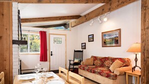Un coin repas chaleureux avec une table en bois dressée pour quatre personnes, un canapé agrémenté de coussins à motifs et une lampe posée sur une table d’appoint.