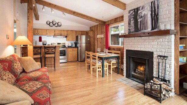 Un salon chaleureux avec une cheminée, des meubles en bois et une cuisine en arrière-plan.