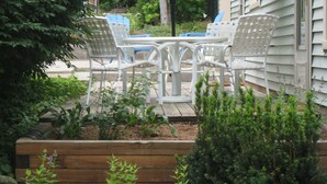 Eine Terrasse mit Tisch und Stühlen, umgeben von Pflanzen und einem grünen Sonnenschirm.