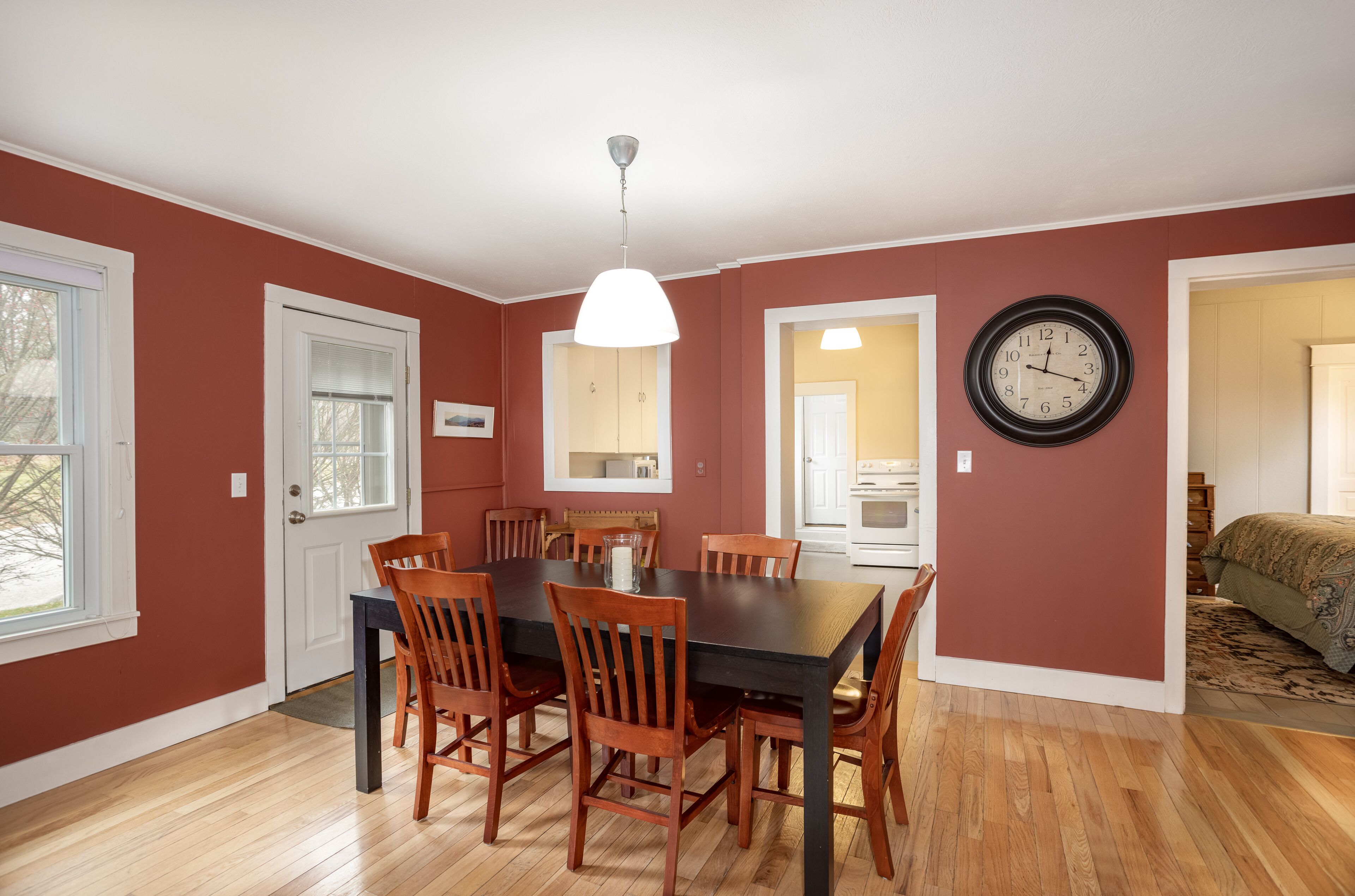 A dining area with a wooden table and chairs, a hanging light fixture, and a wall clock.