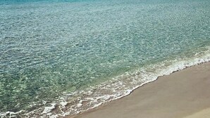 Une jetée s’avançant dans des eaux calmes et limpides, avec une plage de sable au bord.