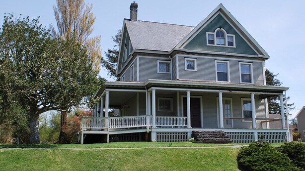 A two-story house with a front porch, a chimney, and a large tree in the yard. - Commanders Quarters Historic Home in Hammond – Sleeps 18 (Hammond)