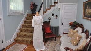 A staircase with floral carpet, a white dress on a mannequin, a red chair, and a white sofa with floral cushions. - Commanders Quarters Historic Home in Hammond – Sleeps 18 (Hammond)