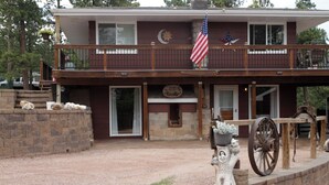 A two-story house with a balcony, an American flag, a stone wall, and a decorative wagon wheel.
