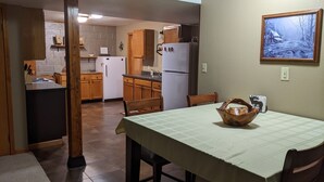 A kitchen with wooden cabinets, a white refrigerator, and a dining table with a green tablecloth.