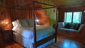 Un lit à baldaquin en bois se trouve dans une chambre de style rustique, avec une fenêtre et un banc placé près de la fenêtre.