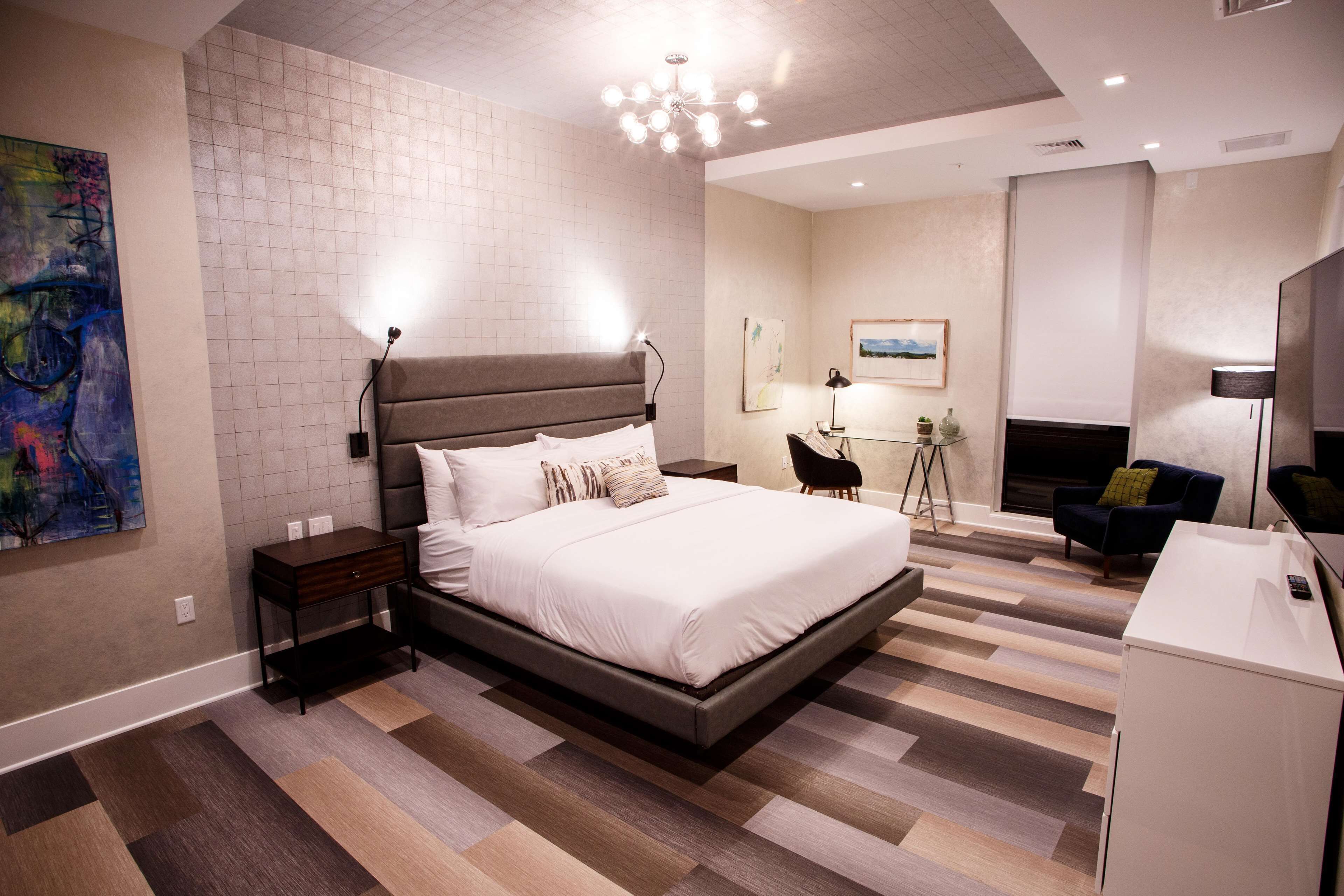 A modern bedroom with a large bed, bedside tables, a desk, and a chair.