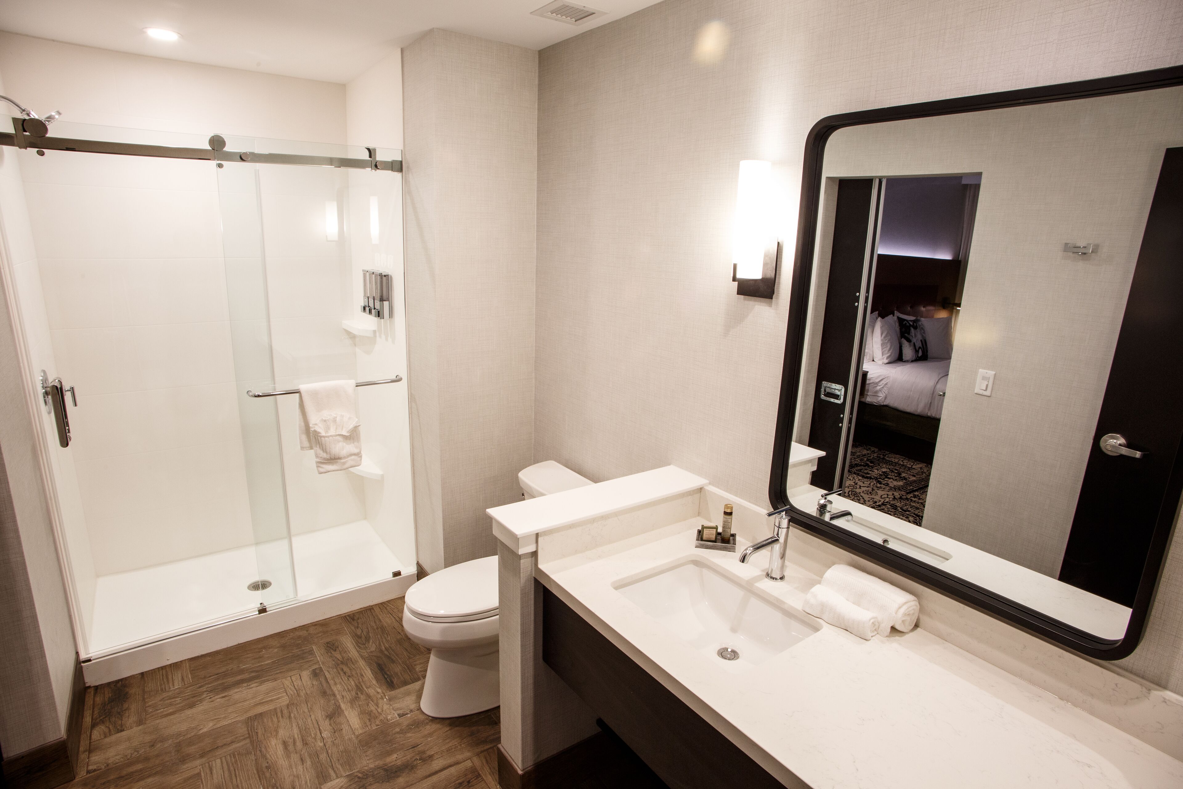 Un baño moderno con ducha de vidrio, inodoro blanco, lavamanos con espejo y barra para toallas.