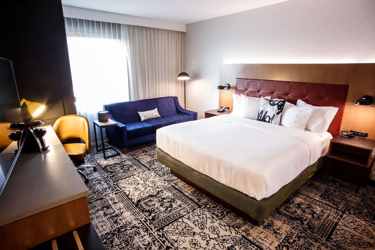 Ein Hotelzimmer mit einem großen Bett, einer Sitzecke, einem Schreibtisch, einem Stuhl, einer Lampe und einem Nachttisch mit Telefon.