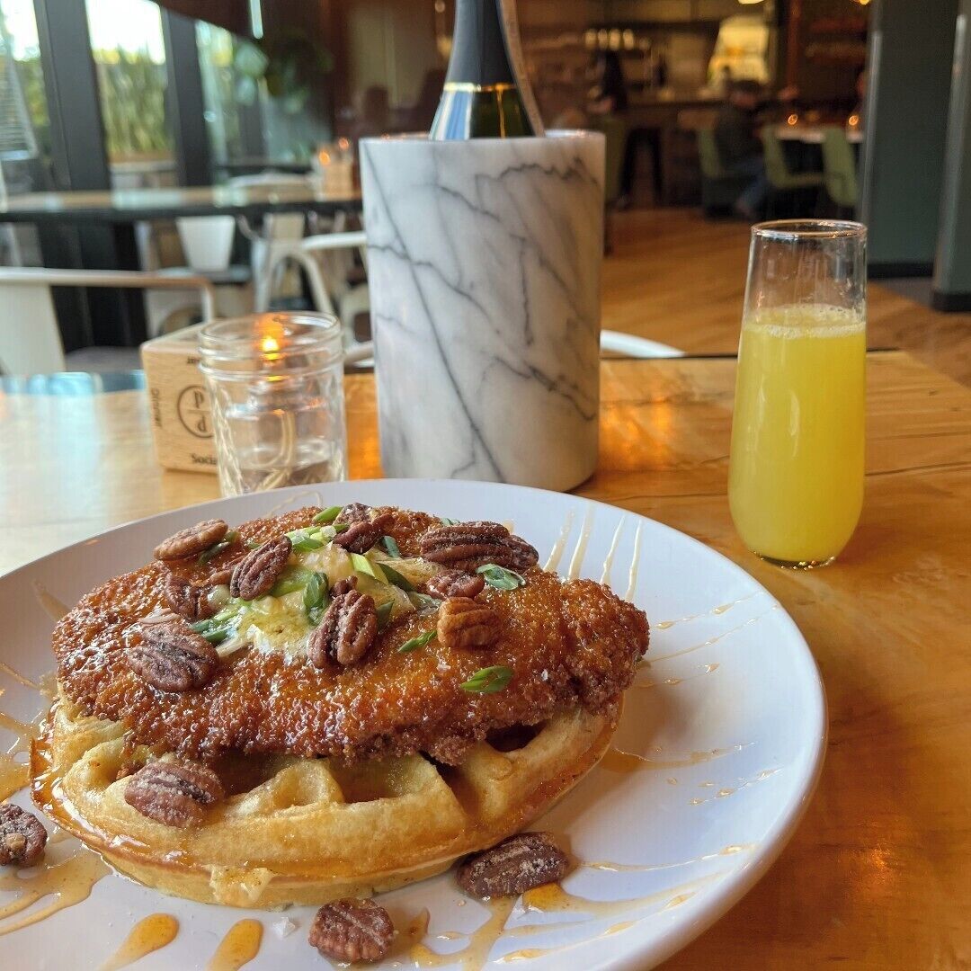 A plate of food with pecans on a white plate, a glass of orange juice, and a marble vase on a wooden table.