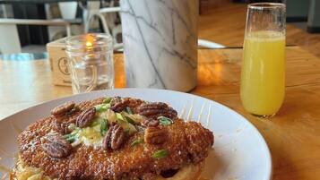 A plate of food with pecans on a white plate, a glass of orange juice, and a marble vase on a wooden table.