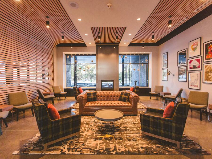 A lobby with a central brown leather sofa, plaid armchairs, and a round coffee table.
