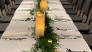 A long dining table with candles, cutlery, and greenery arranged for a formal event.