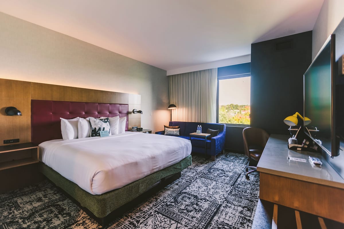 Ein Hotelzimmer mit einem großen Bett, einem Schreibtisch, einem Stuhl, einem Fernseher und einem Fenster mit Aussicht.