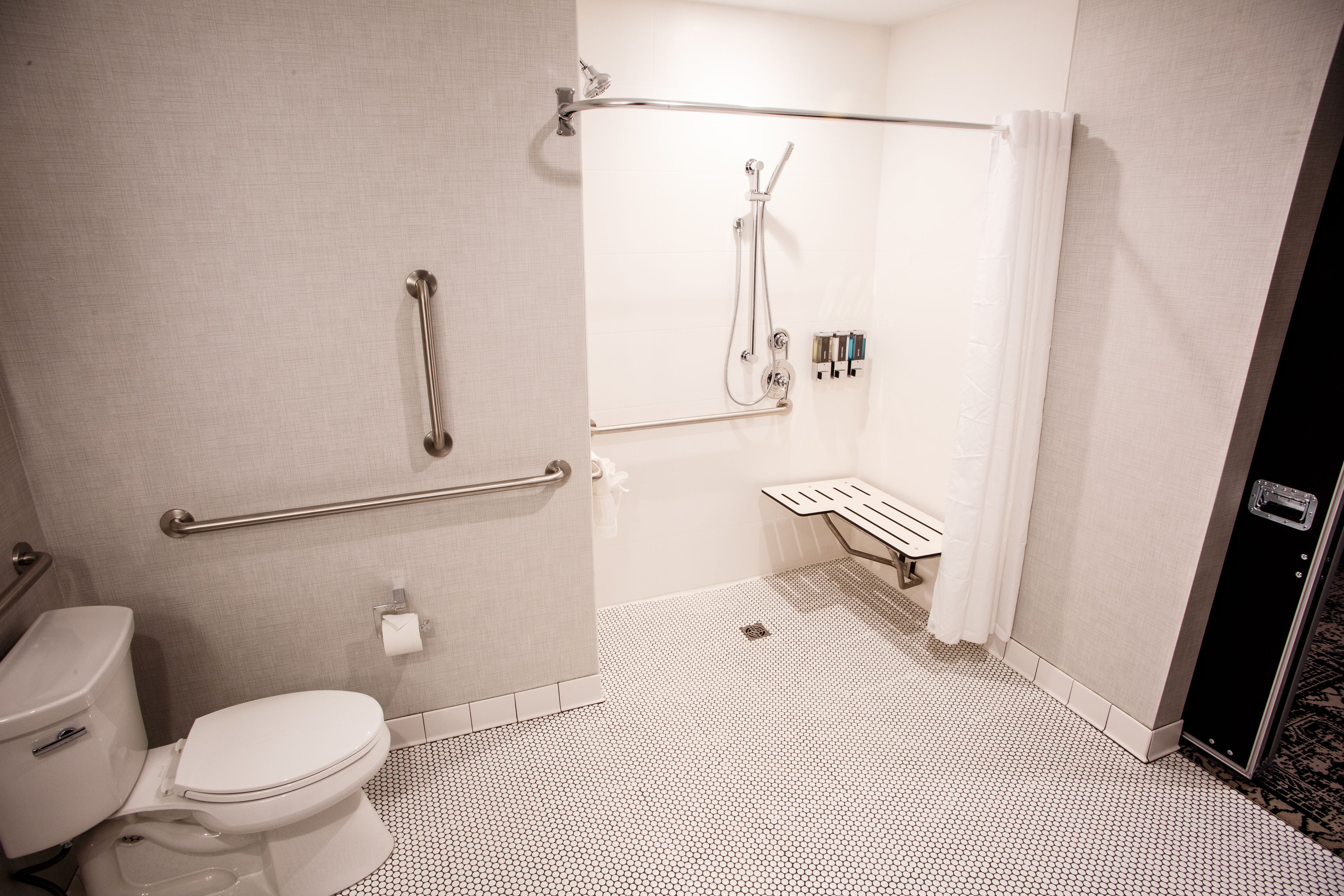 A bathroom with a toilet, a shower with a grab bar, and a hand dryer.
