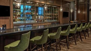 Zona de bar con varios taburetes, una barra y una variedad de botellas y vasos.