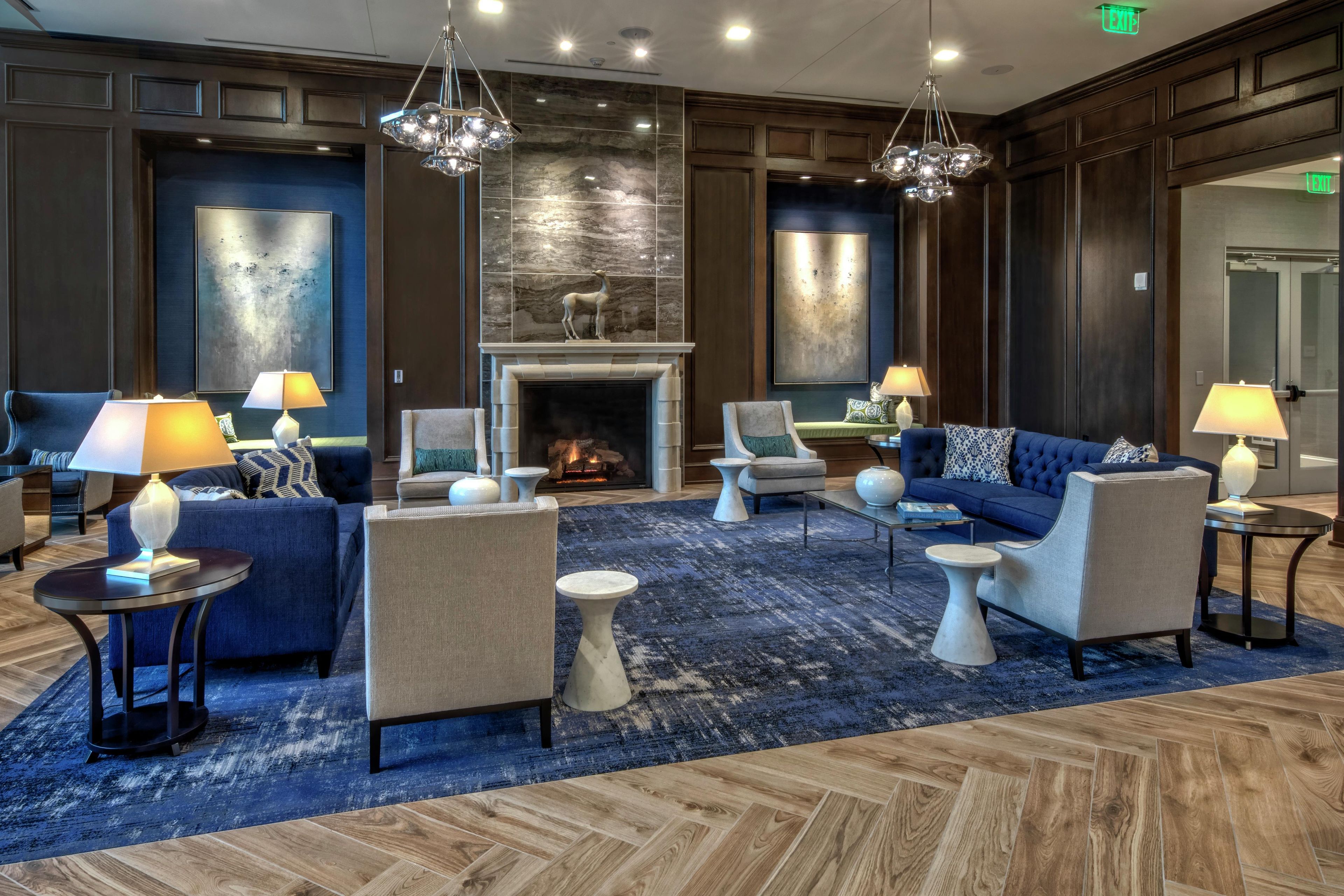 A hotel lobby with a fireplace, seating arrangements, and a blue carpet.