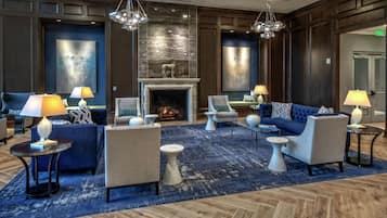 A hotel lobby with a fireplace, seating arrangements, and a blue carpet.