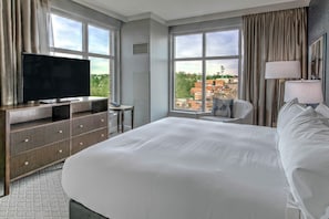Ein Hotelzimmer mit einem grossen Bett, einem Flachbildfernseher, einem Schreibtisch mit Stuhl und Blick auf die Stadt durch grosse Fenster.