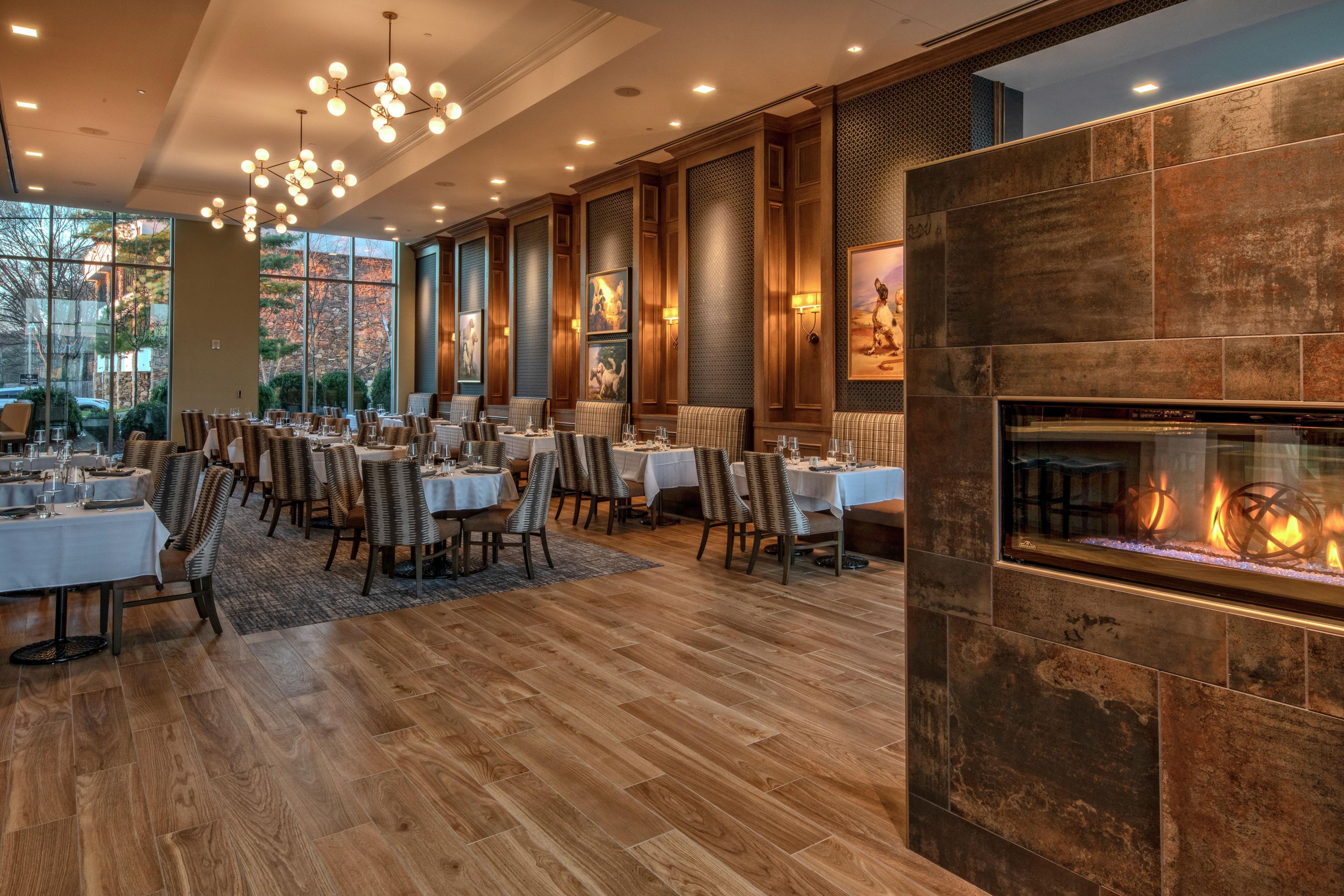 Un vaste espace dédié à la salle à manger, avec plusieurs tables et chaises, une grande fenêtre offrant une vue sur l’extérieur et une cheminée au design moderne.