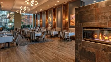 Un vaste espace dédié à la salle à manger, avec plusieurs tables et chaises, une grande fenêtre offrant une vue sur l’extérieur et une cheminée au design moderne.