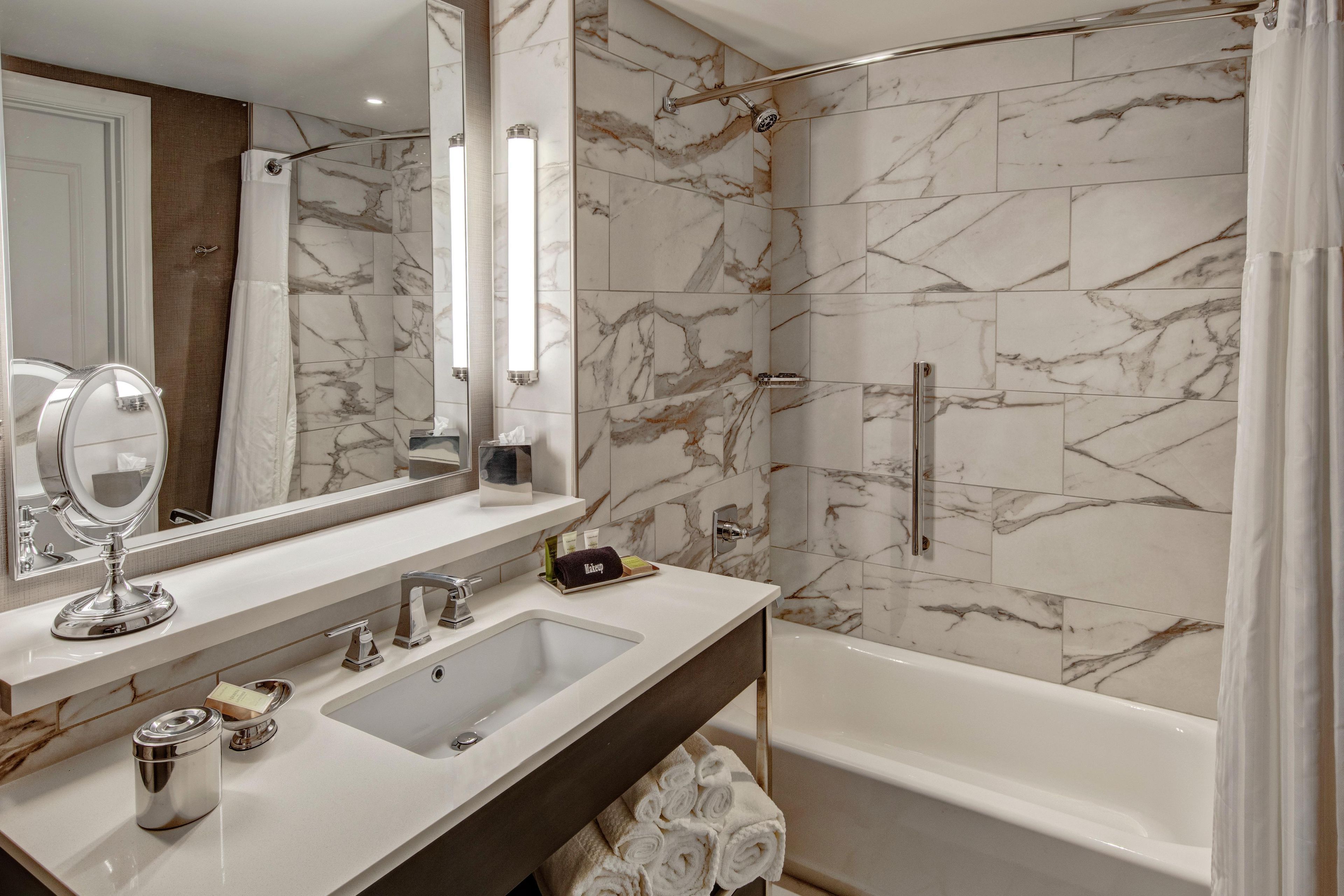 A bathroom with a marble wall, a sink, a mirror, a shower, and a bathtub.