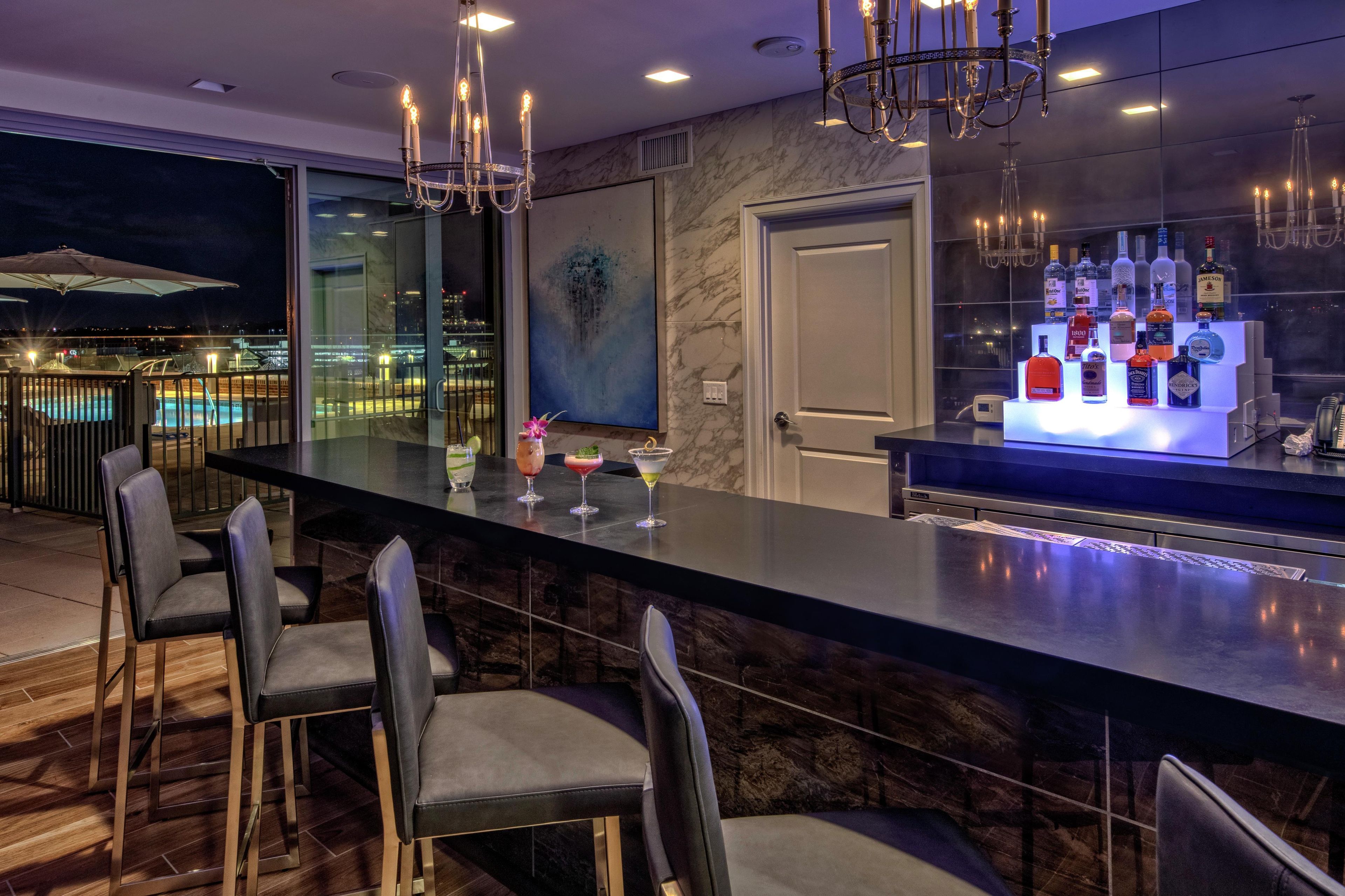 A modern bar area with a marble countertop, bar stools, and a view of the city at night.