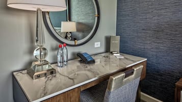 A hotel room with a marble desk, a mirror, a lamp, a telephone, and a water bottle.