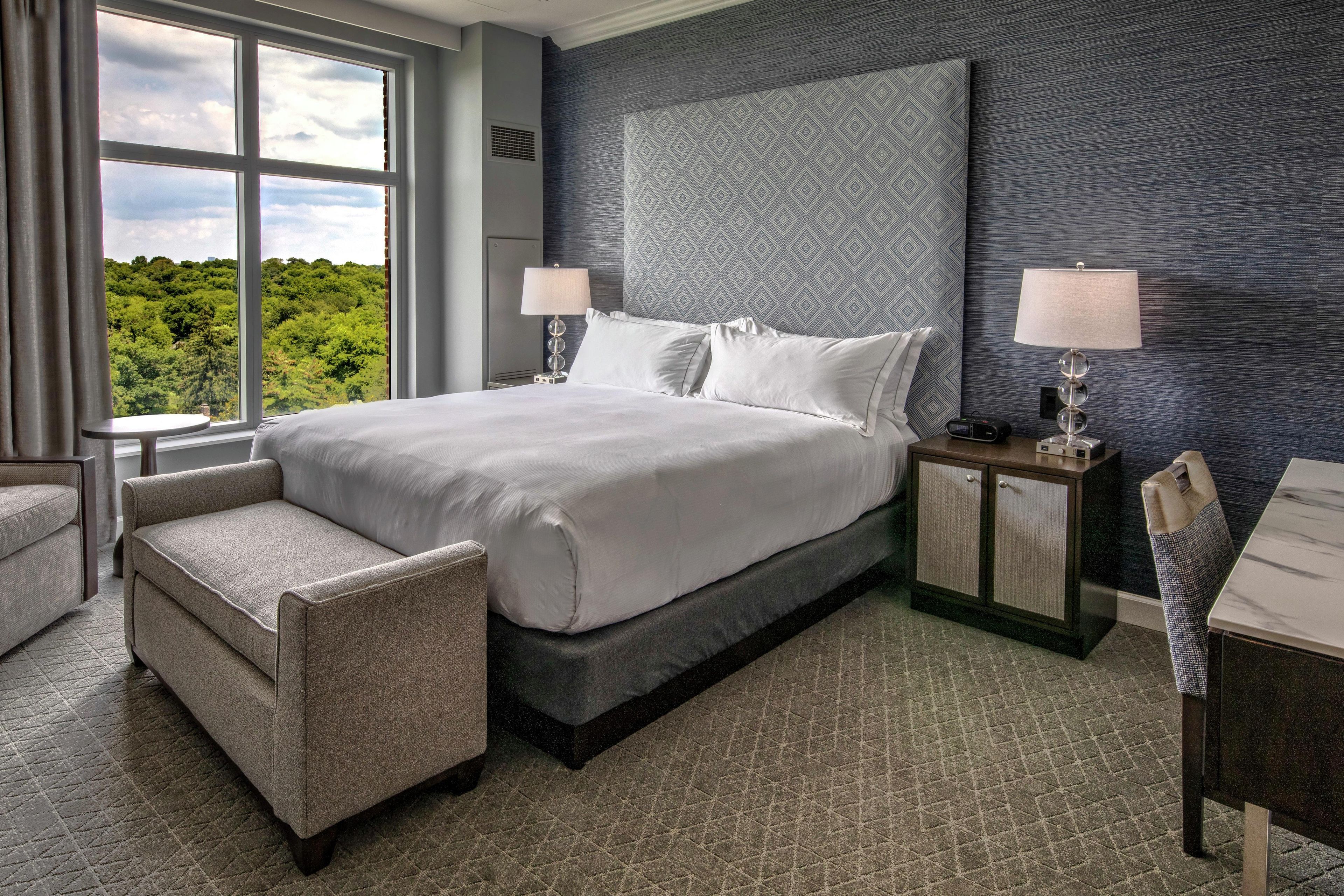 A hotel room with a large bed, two bedside tables, a chair, and a view of the outdoors.