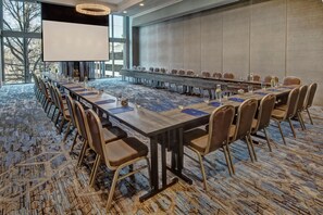 Konferenssihuone, jossa on pitkä pöytä, tuoleja ja projektorikangas.