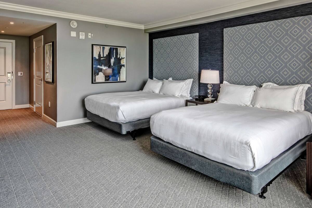 Una habitación de hotel con dos camas, una obra de arte grande en la pared, un cabecero estampado y suelo cubierto de alfombra.