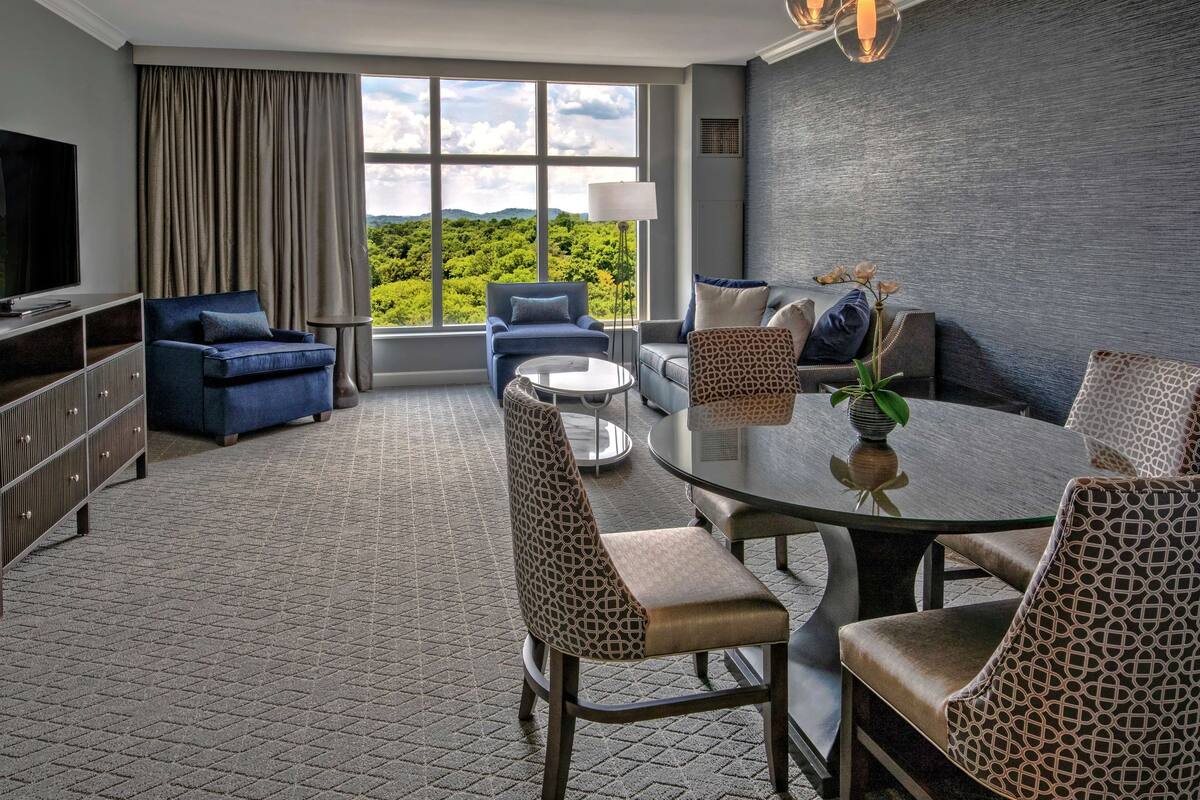 Una habitación de hotel moderna con un ventanal grande, una mesa de comedor y asientos cómodos.