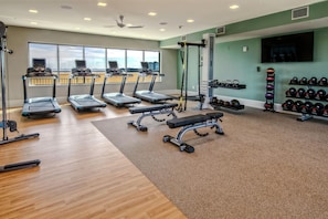 Ein Fitnessraum mit Laufbändern, einer Hantelbank und einem Wand-Fernseher.
