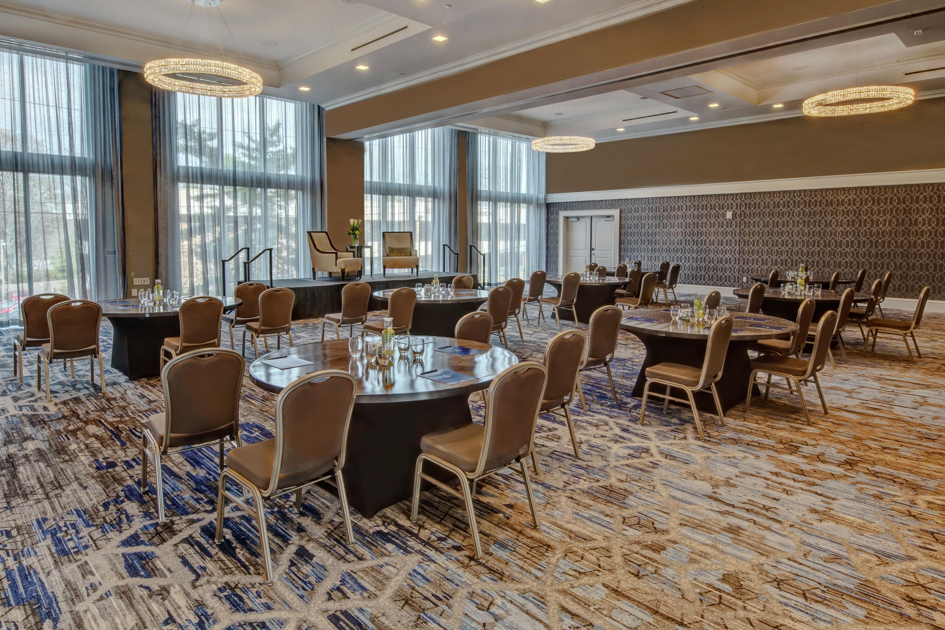 A conference room with round tables and chairs, large windows, and a patterned carpet.