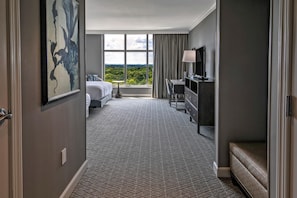 Een hotelkamer met een bed, bureau, stoel, televisie en een groot raam met uitzicht op de omgeving.