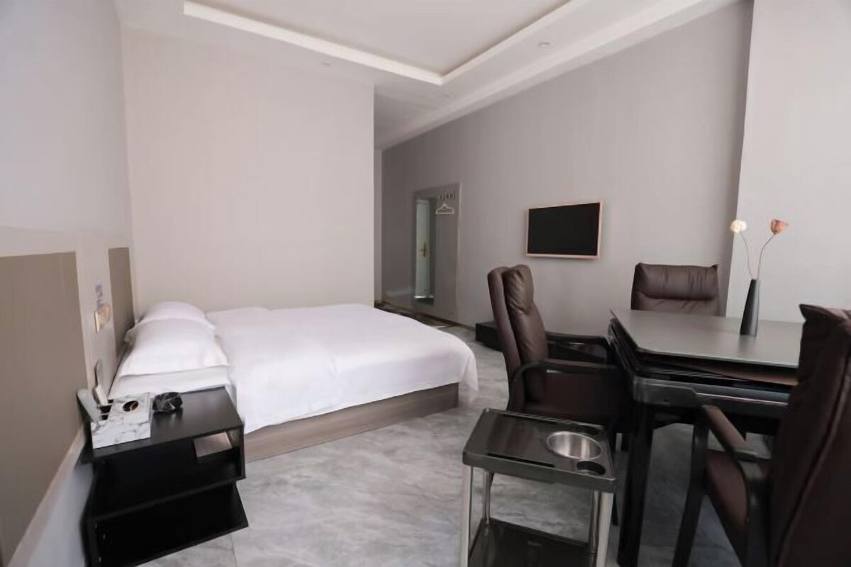 A modern hotel room with a bed, a desk, a chair, and a small table.