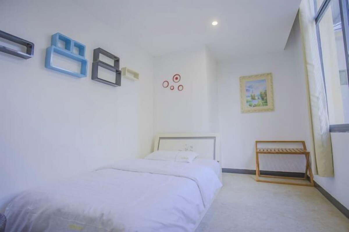 A bedroom with a bed, a wooden bench, a painting, and wall-mounted storage units.