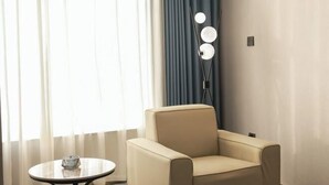 A room with a beige armchair, a small round table with a glass object, and a floor lamp with three lights. - Langting Boutique Hotel (Ruili)