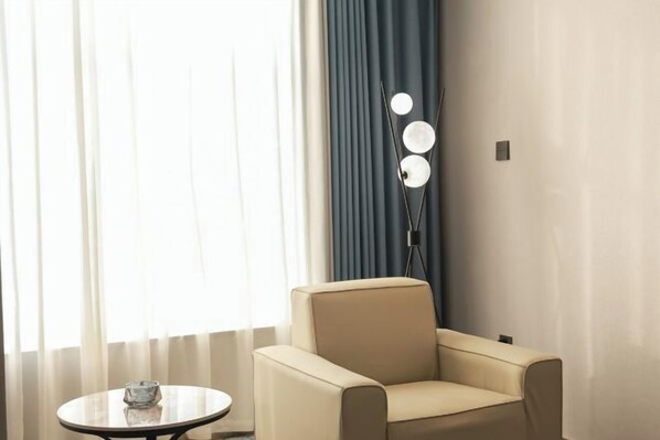 A room with a beige armchair, a small round table with a glass object, and a floor lamp with three lights. - Langting Boutique Hotel (Ruili)