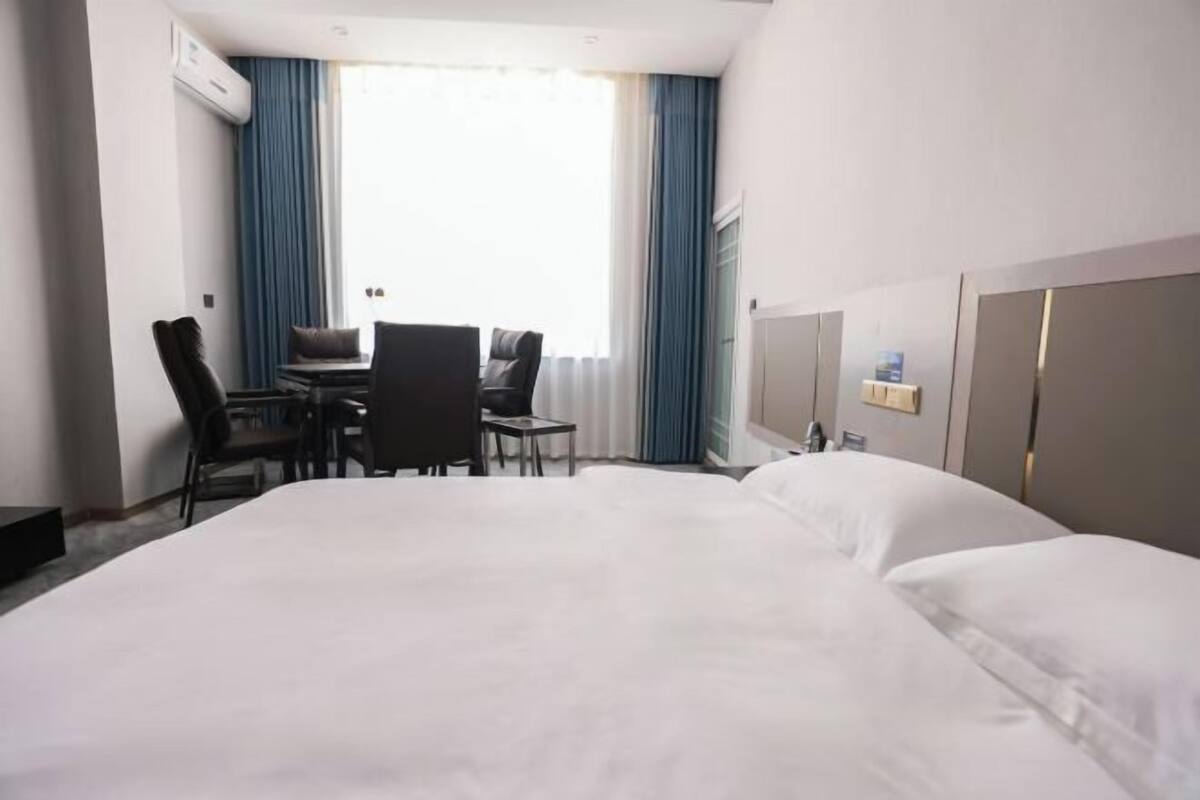 Hotellihuone, jossa on suuri sänky, työpöytä tuolilla sekä ikkuna, jossa on verhot.