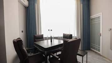 Una habitación con una mesa rectangular, cuatro sillas, una ventana con cortinas y un equipo de aire acondicionado.