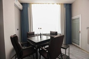 A room with a rectangular table, four chairs, a window with curtains, and an air conditioning unit.