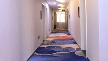 Un pasillo de hotel con alfombra estampada, puertas a ambos lados y una fuente de luz al final.