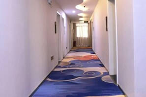 Un pasillo de hotel con alfombra estampada, puertas a ambos lados y una fuente de luz al final.