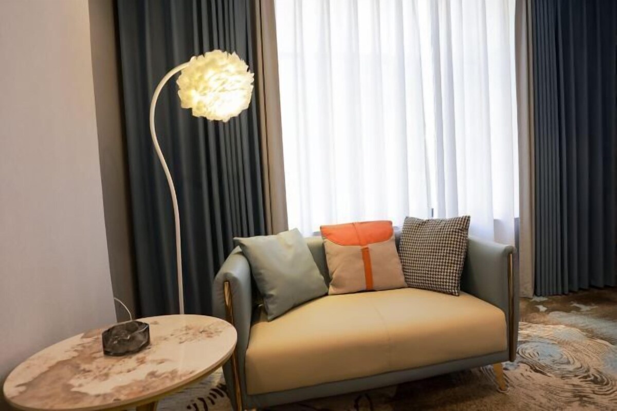 A sofa with cushions, a floor lamp, and a small table in a room with curtains and a carpet.