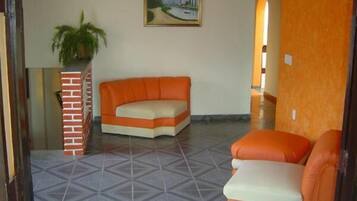 Uma sala de estar com um sofá e uma poltrona, um vaso de plantas e um quadro na parede.