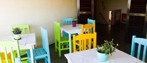 A dining area with colorful chairs and tables, a potted plant on each table, and a brick fireplace in the background.