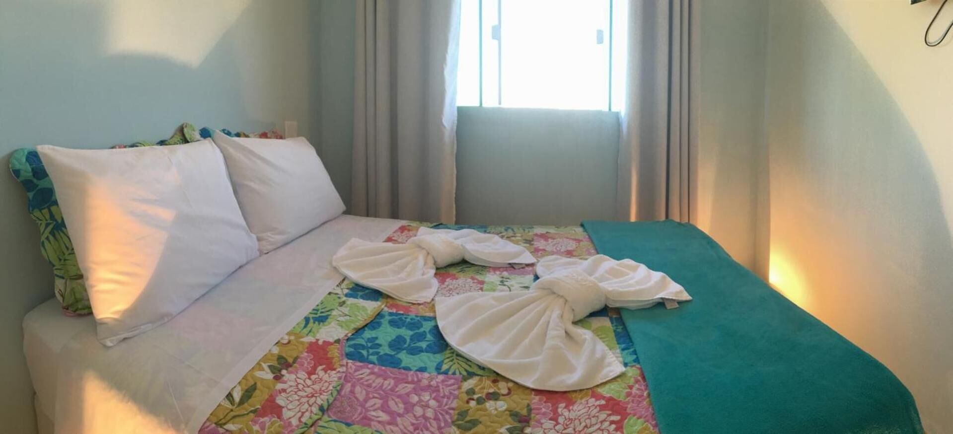 A bed with a colorful quilt, white pillows, and a teal blanket.