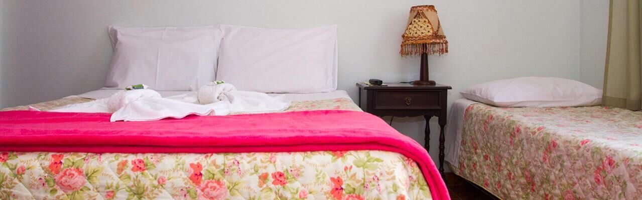 A hotel room with a large bed, two smaller beds, a nightstand, and a lamp.